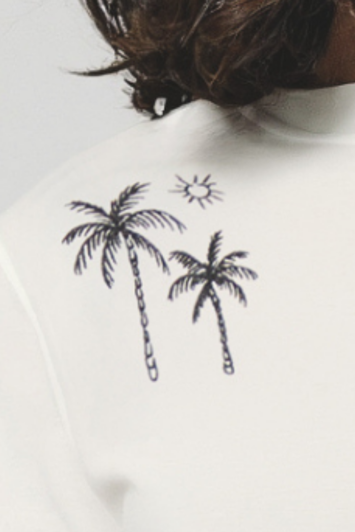 Close up of white shirt with black palm tree and sun design on a plain background.