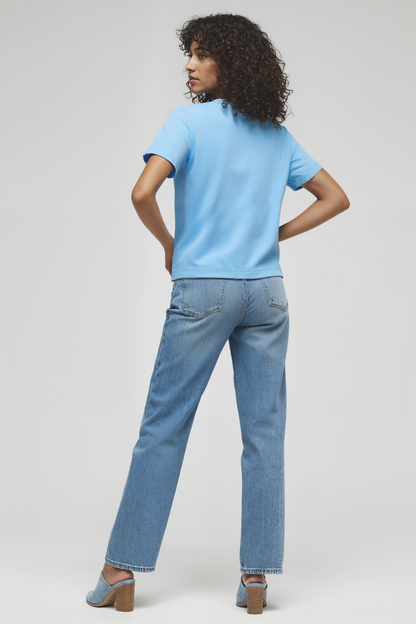 Back view of woman wearing a light blue shirt and jeans on a white background