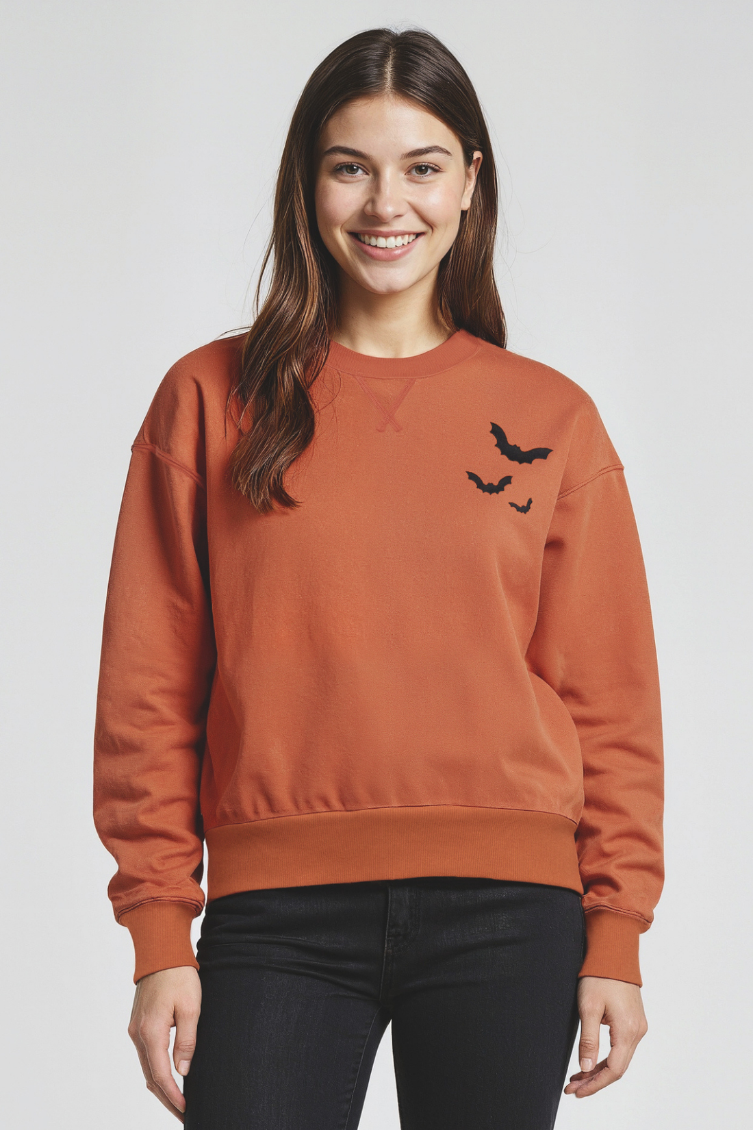 Woman wearing a orange sweatshirt with 3 black bats designs, on left shoulder on a white background.