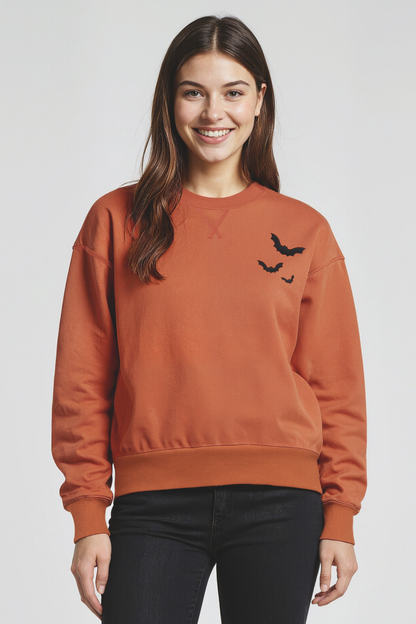 Woman wearing a orange sweatshirt with 3 black bats designs, on left shoulder on a white background.