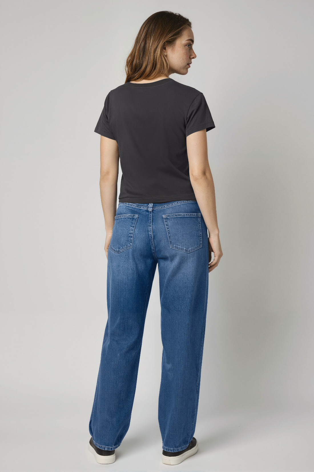 Woman wearing a black t-shirt and blue jeans against a plain background