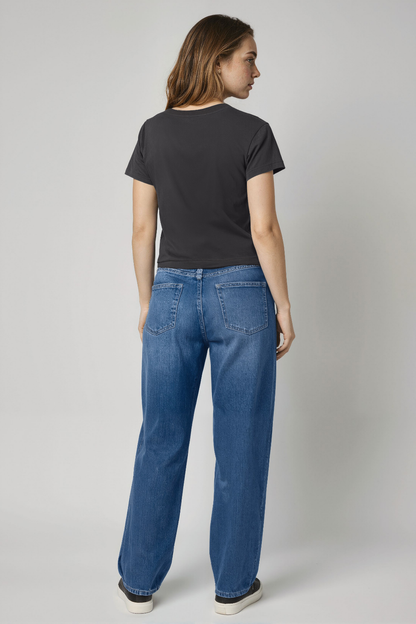 Woman wearing a black t-shirt and blue jeans against a plain background