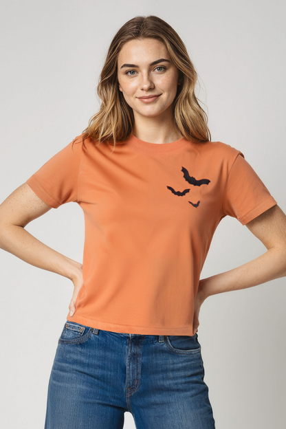 Woman wearing an orange t-shirt with a 3 black bats design on a plain background.