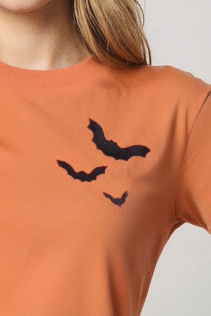 Close up of front of orange t-shirt with 3 black bats designs on a plain background