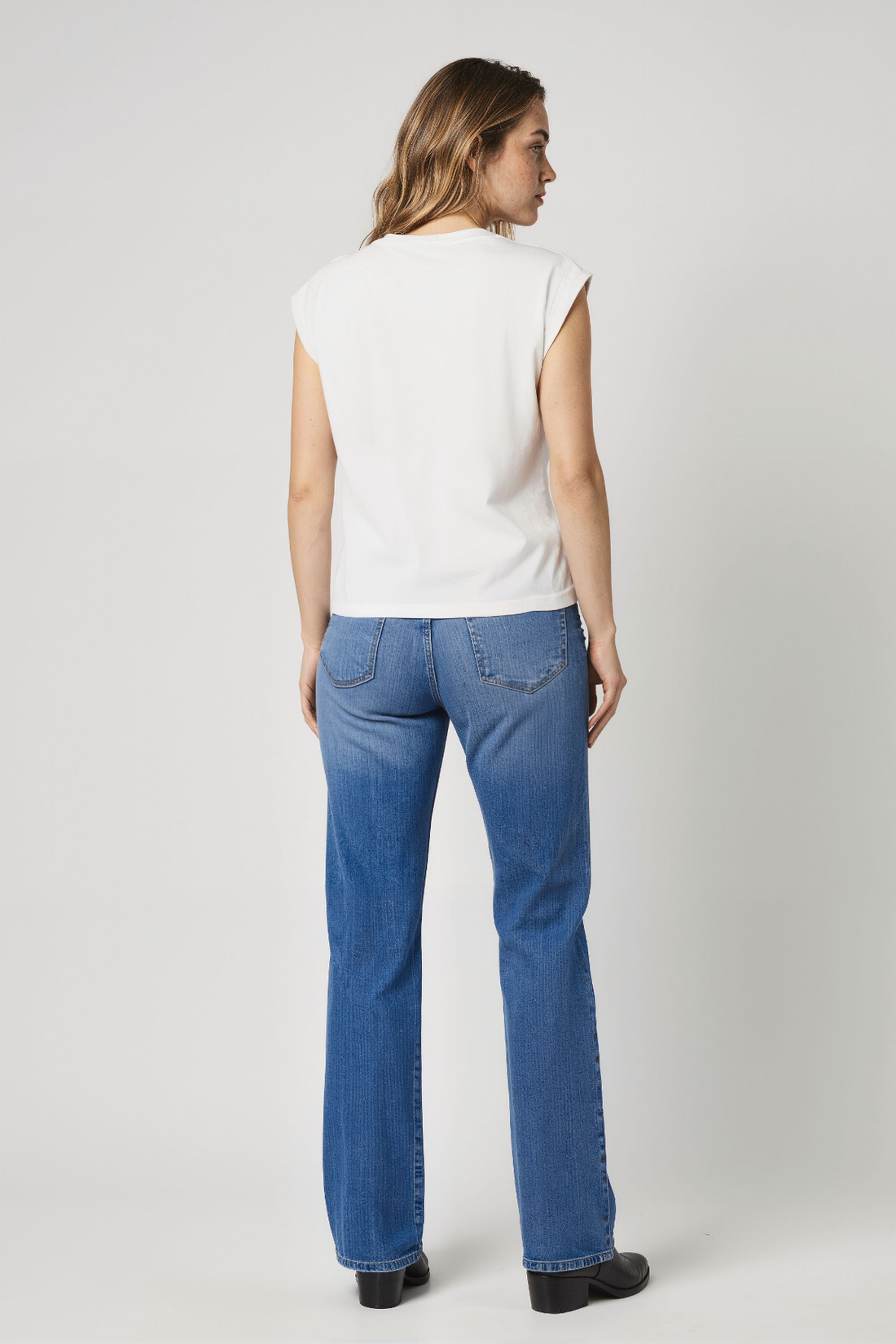 Woman wearing a white sleeveless top and blue jeans on a plain background.