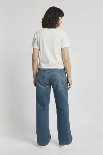 Back of woman wearing a white t-shirt and blue jeans on a plain background