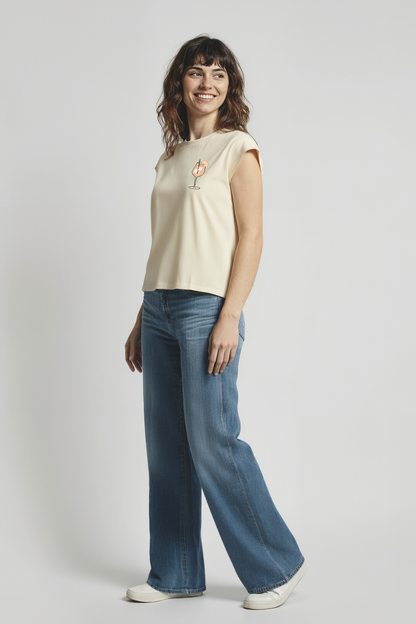 Woman wearing a yellow tank with a small cocktail drink glass graphic and jeans on a plain background
