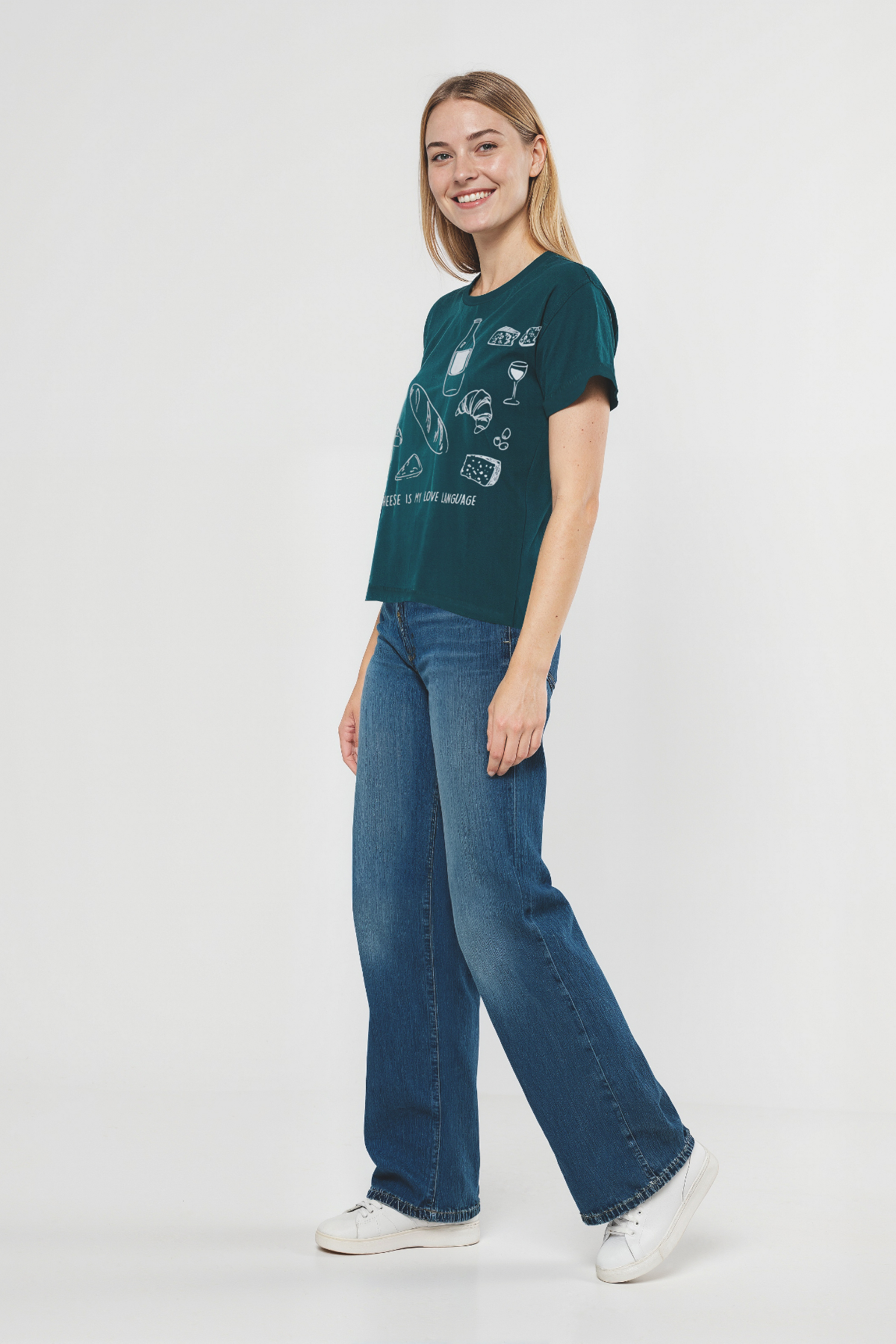 Woman wearing a teal t-shirt with white illustrations of cheese, wine, and bread, and text &