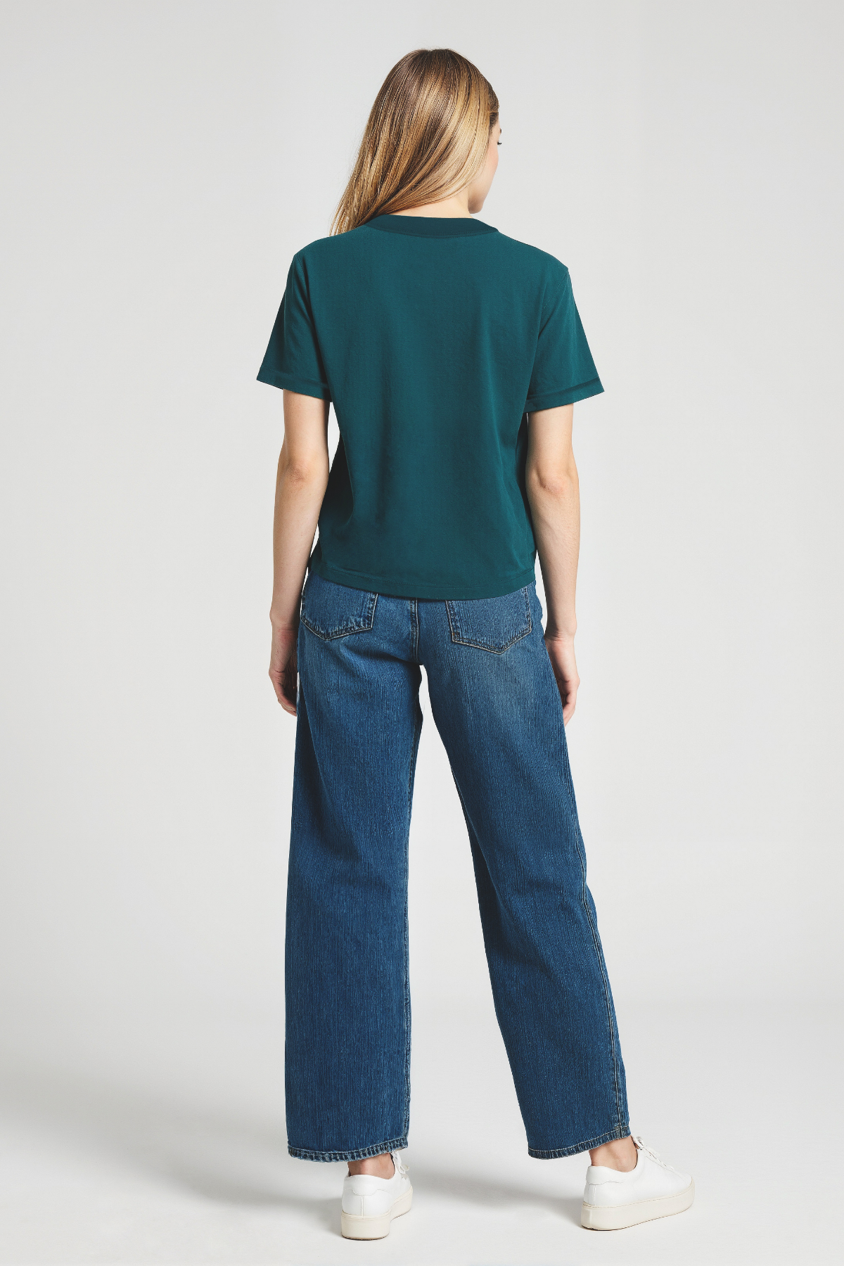 Back of woman wearing a teal t-shirt and blue jeans on a white background
