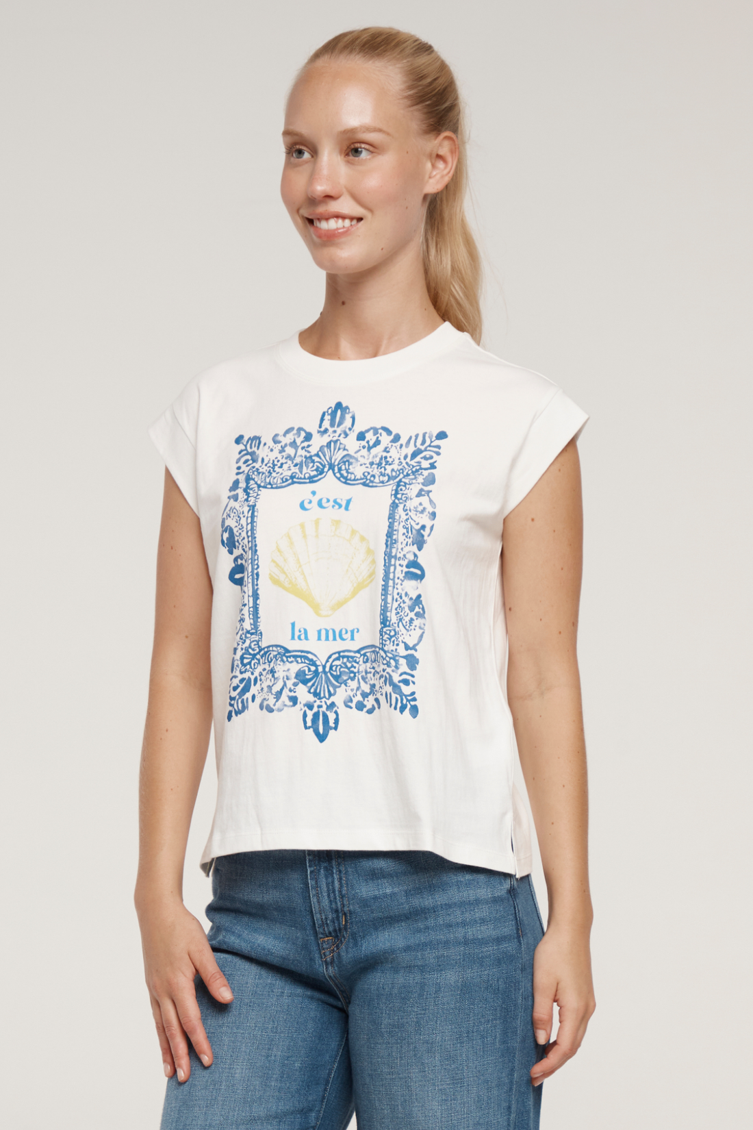 Woman wearing white t-shirt with blue frame graphic design featuring a yellow shell and &