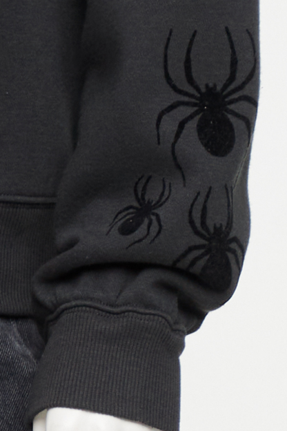 Close up of black hoodie with spider designs on lower left sleeve cuff on a white background