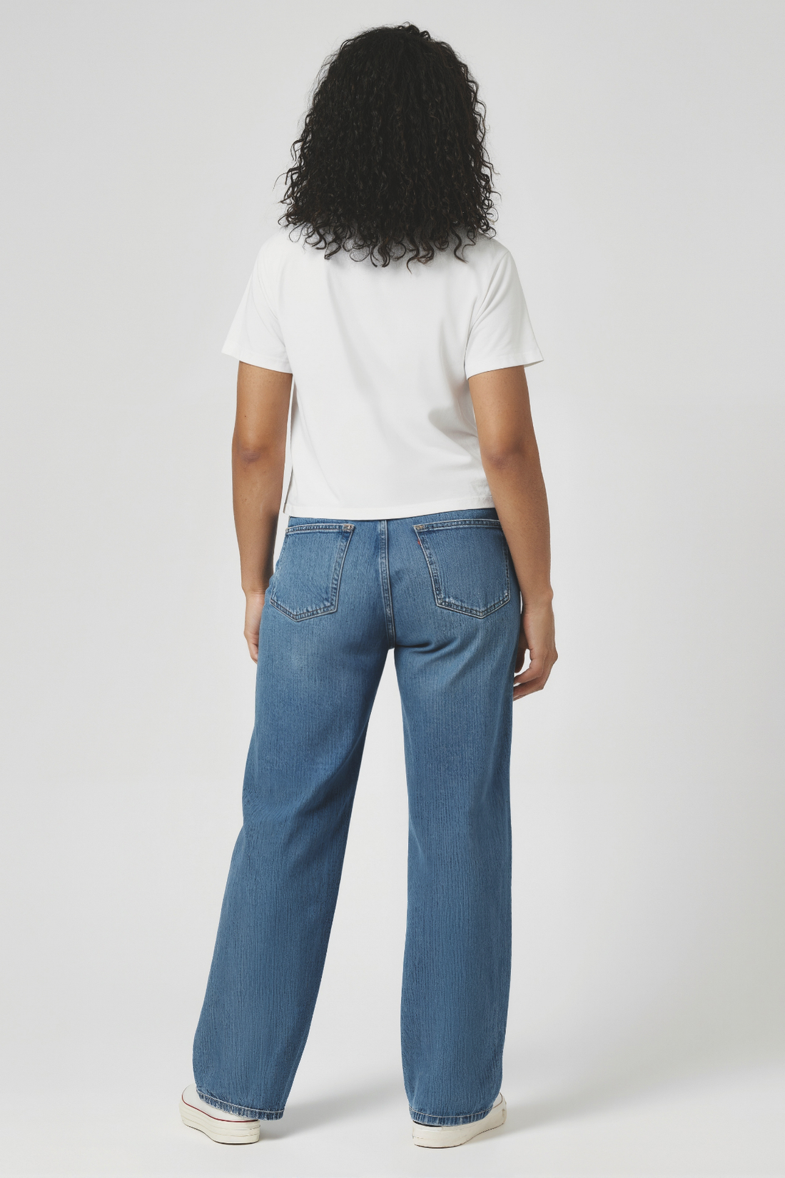 Back of woman wearing a light blue t-shirt and blue jeans on a white background