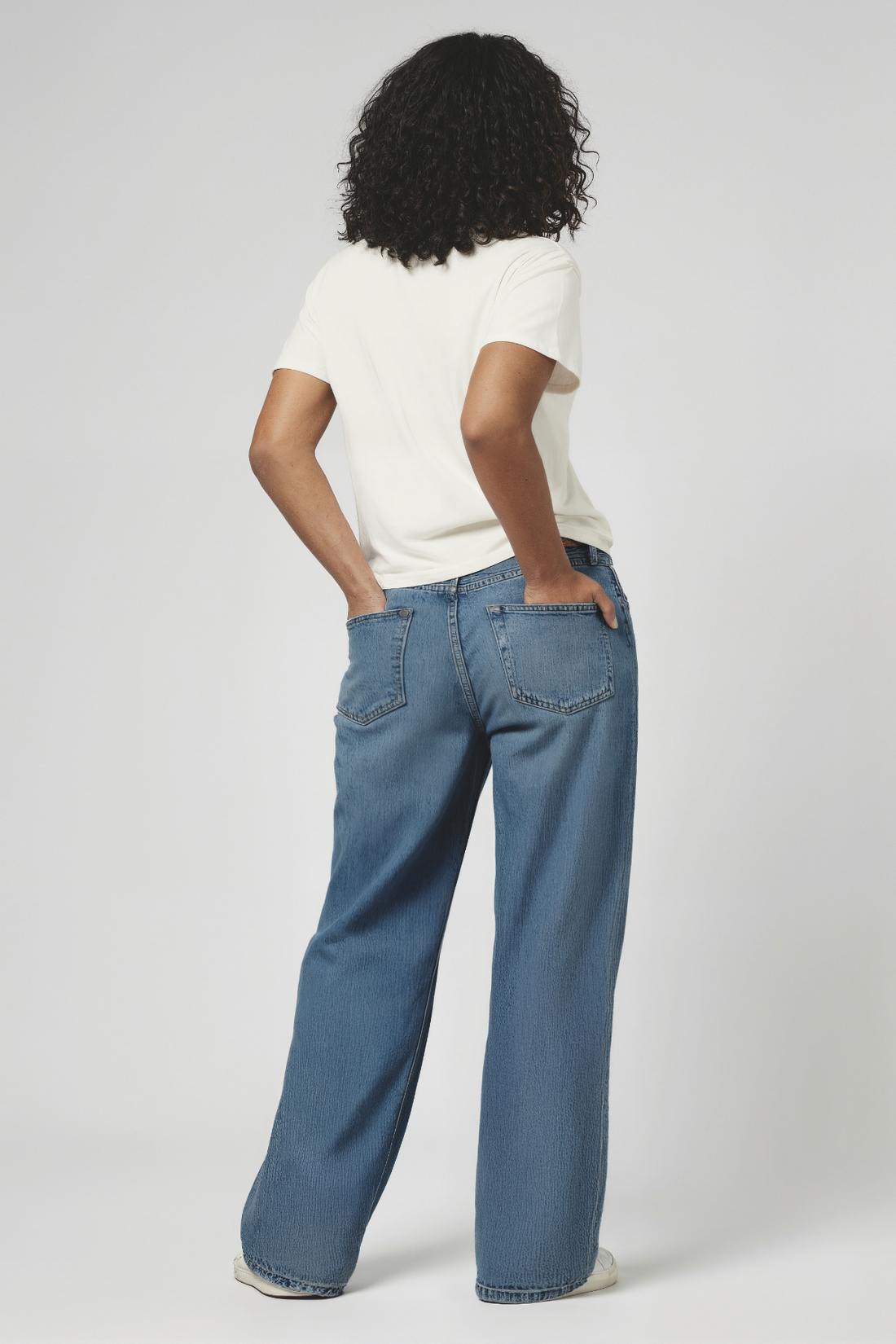 Back of woman wearing blue jeans and a white shirt on a plain background