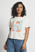 Woman wearing white t-shirt with a colorful graphic of a wine glass and &