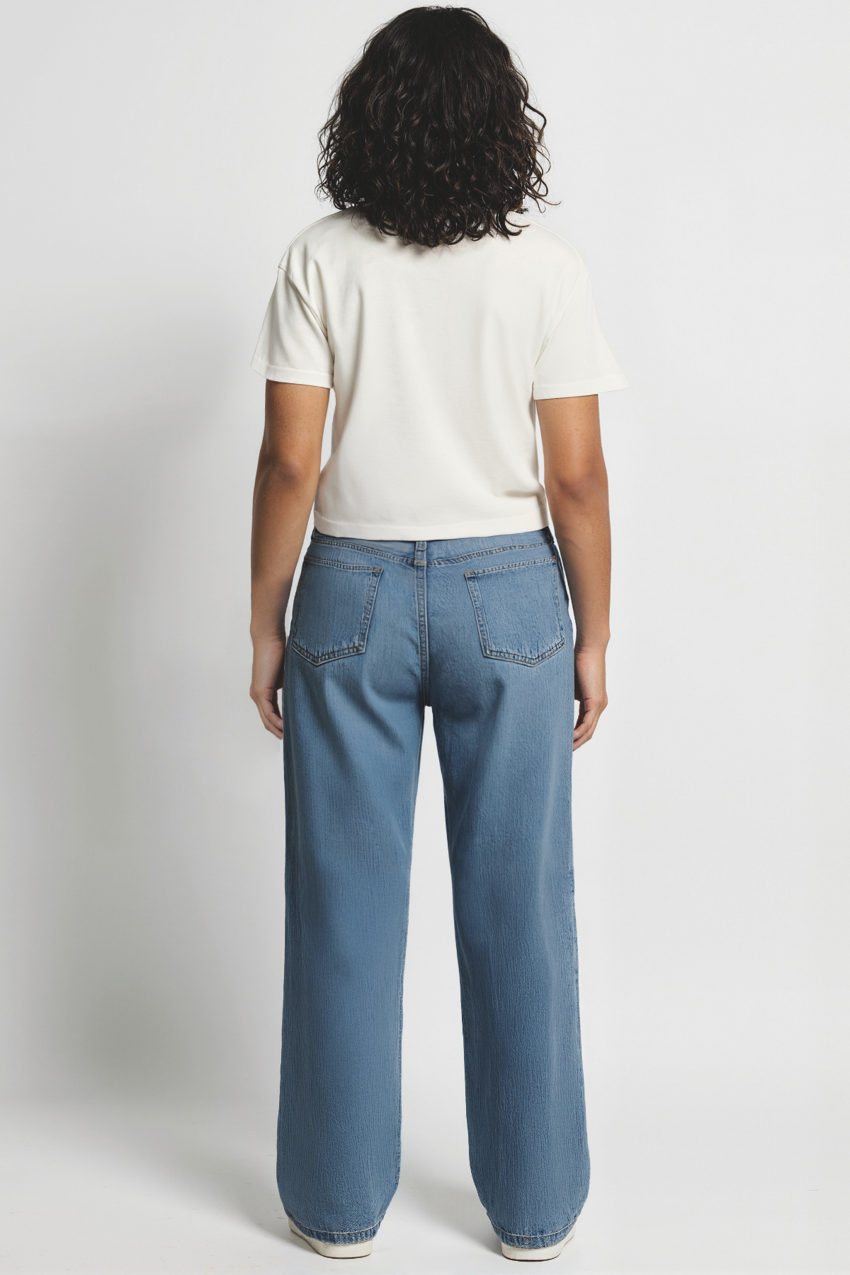 Back of woman wearing a white t-shirt and blue jeans on a plain background