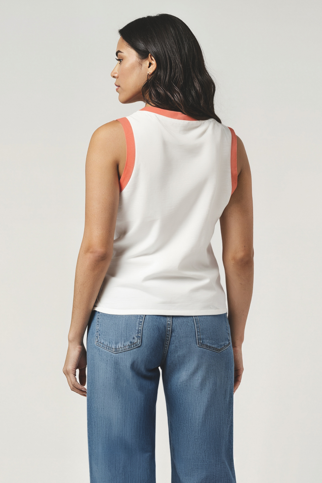 Back of woman wearing a white tank with orange sleeve hems and blue jeans on a white background