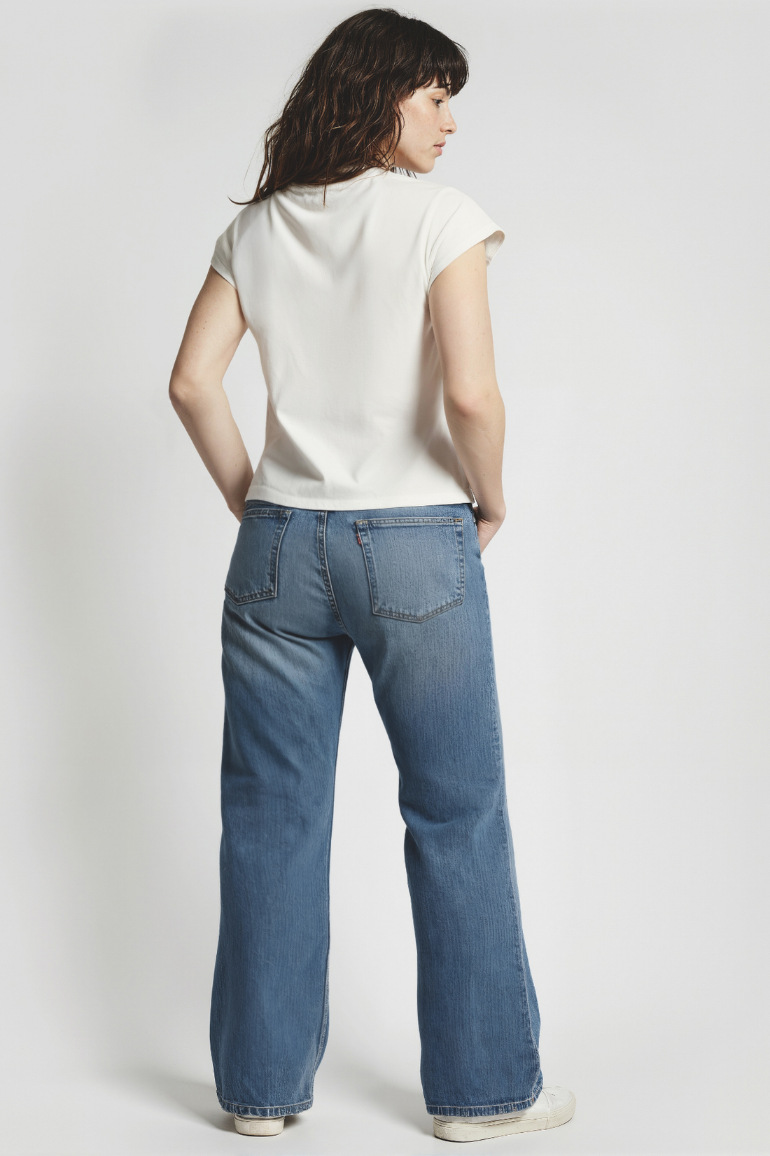 Back of woman wearing a white t-shirt and blue jeans on a white background