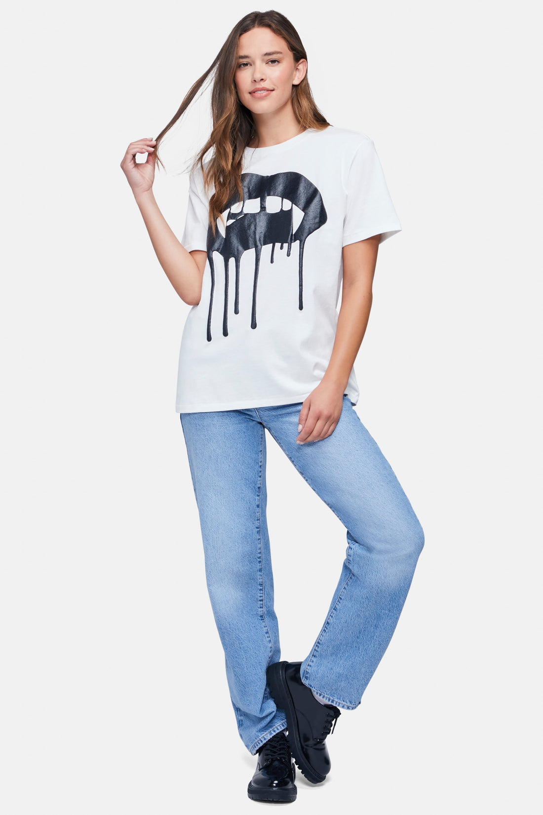 A woman wearing a white t-shirt with the black large vampire lips with drips graphic paired with denim jeans.