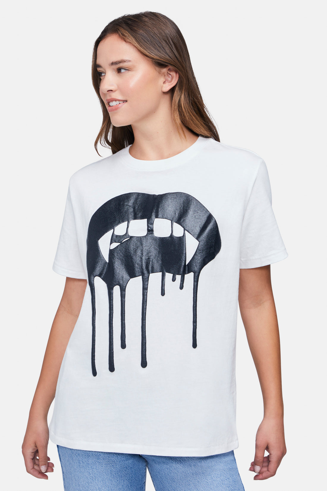 A woman wearing a white t-shirt with the black large vampire lips with drips graphic paired with denim jeans.
