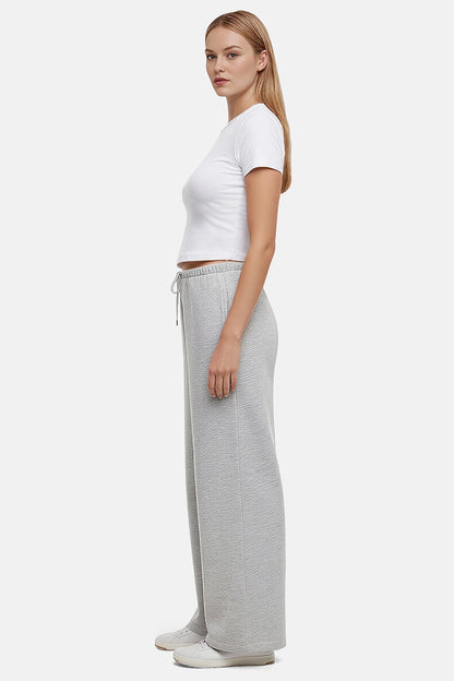Side view of woman wearing a white cropped t-shirt and heather grey wide-leg drawstring sweatpants on a white background
