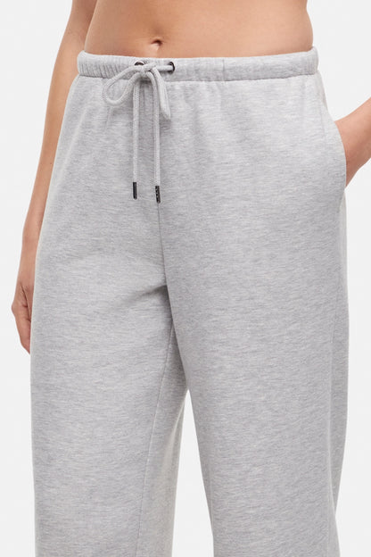 Close up of woman wearing t-shirt and heather grey wide-leg drawstring sweatpants with hand in pocket on a white background