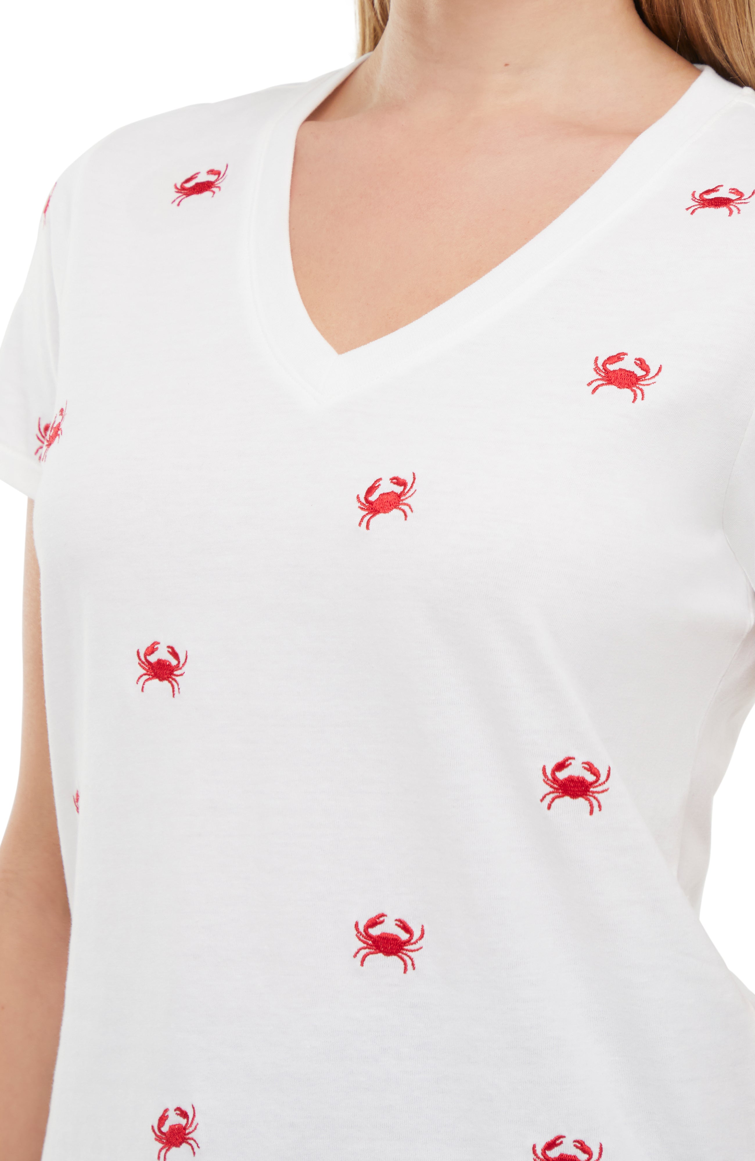 Close up of white top with embroidered red crab patterns worn by a person