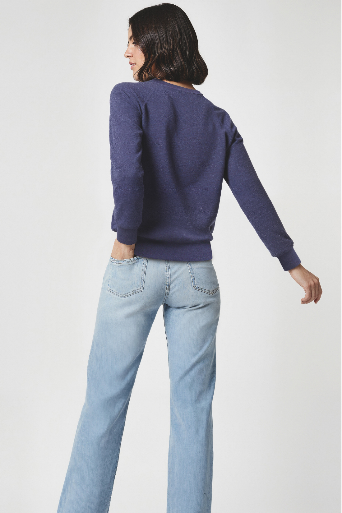 Back of woman wearing a navy sweater and light blue jeans on a white background