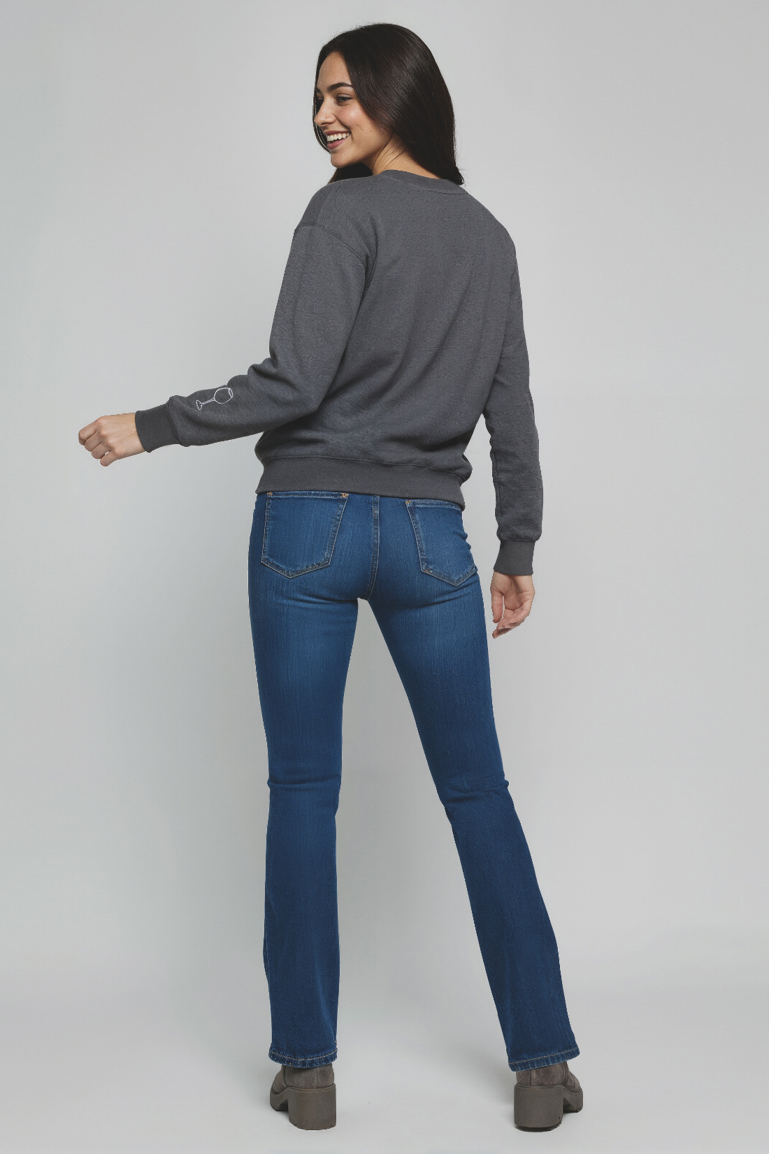 Woman wearing a gray sweater and blue jeans on a plain background