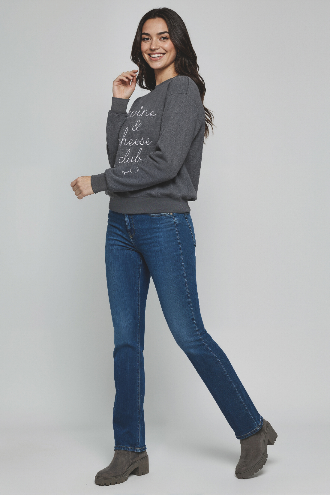 Woman wearing a gray sweatshirt and blue jeans on a plain background