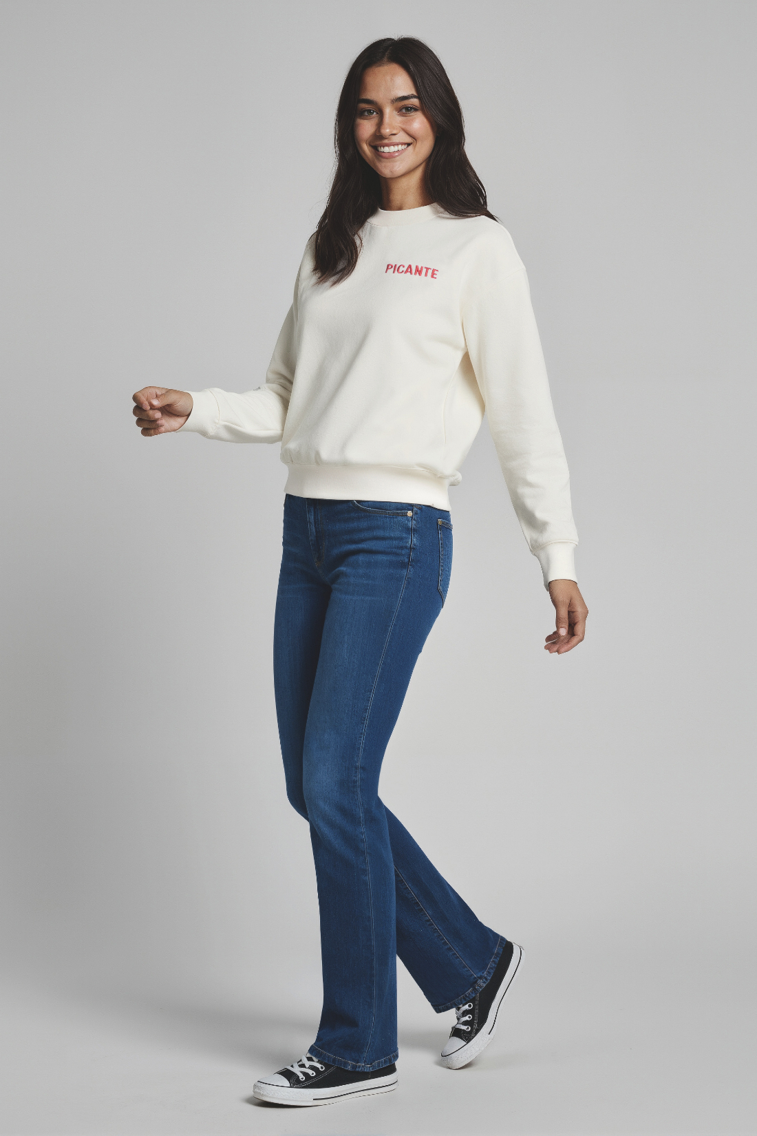 Woman wearing a white sweater with text and blue jeans on a gray background