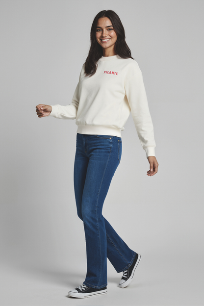 Woman wearing a white sweater with text and blue jeans on a gray background