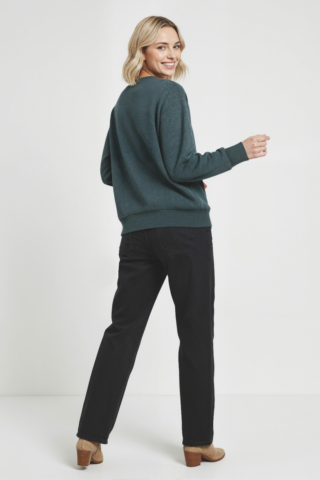 Back of woman wearing a green sweatshirt and black pants on a white background