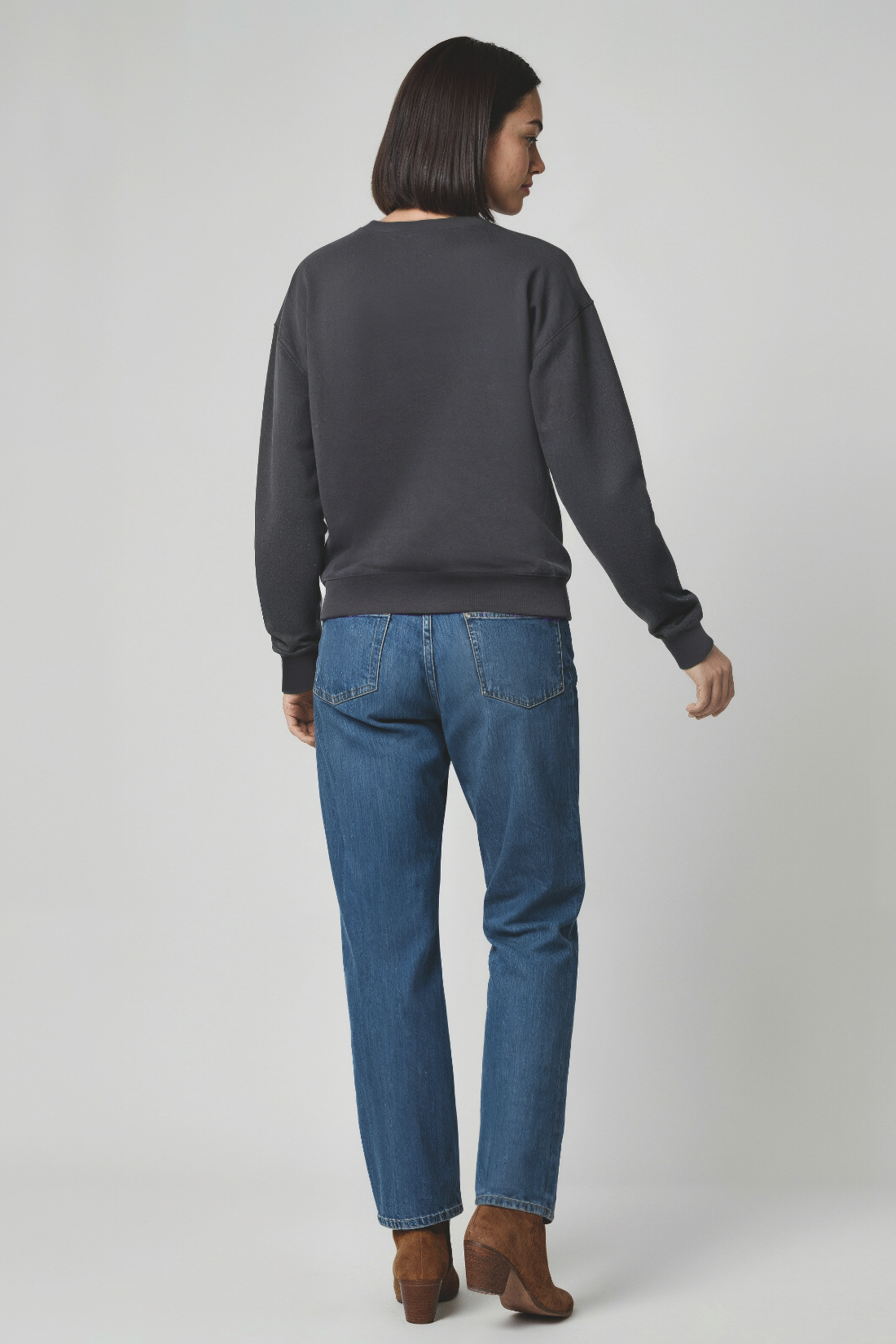 Woman wearing a dark gray sweatshirt and blue jeans on a white background
