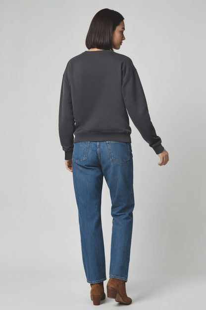 Woman wearing a dark gray sweatshirt and blue jeans on a white background