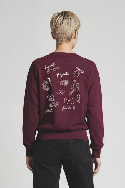 Back of woman wearing a maroon sweatshirt with Italian word designs on the back against a plain background