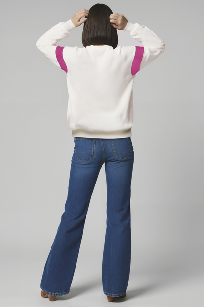 Back of woman wearing a white sweater with purple accents and blue jeans on a white background