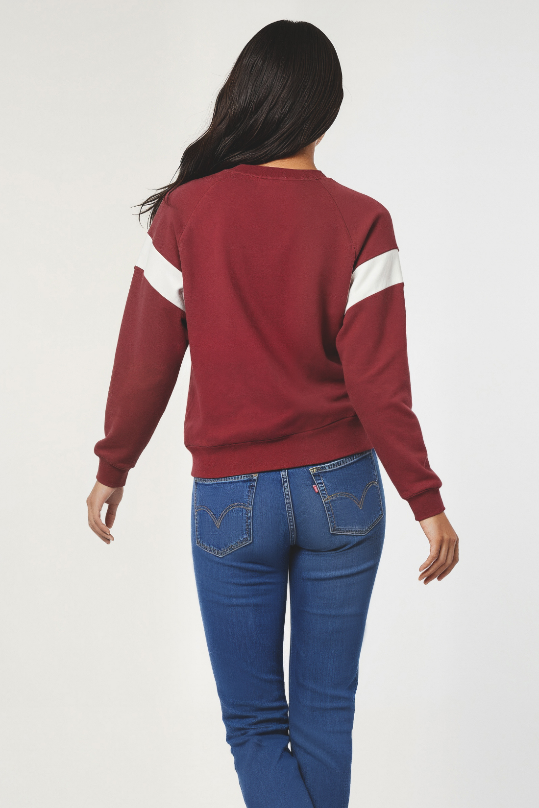 back of woman wearing a red and white long-sleeve shirt and blue jeans on a plain background