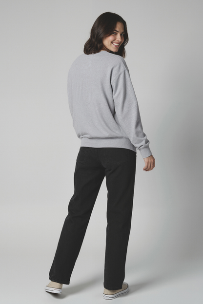 Back of woman wearing a gray sweatshirt with black jeans on a plain background