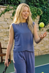 Woman in blue top and matching pants on a tennis court with a tennis ball. 