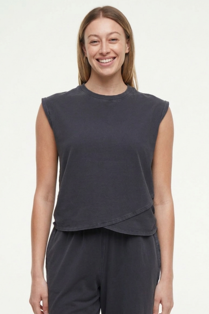 Front view of woman wearing a dark gray sleeveless asymmetrical top and pants on a white background. 