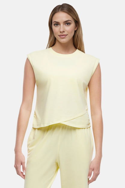 Front view of woman wearing a light-yellow sleeveless asymmetrical top and pants on a white background. 