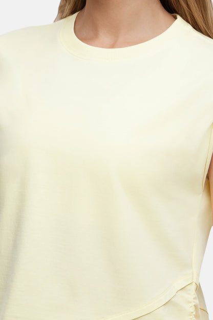 Front close up view of woman wearing a light-yellow sleeveless asymmetrical top and pants on a white background. 