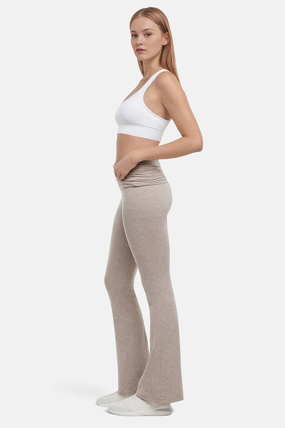 Side view of woman wearing a white sports bra and beige yoga pants on a white background