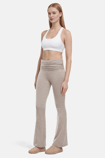 Side view of woman wearing a white sports bra and beige yoga pants on a white background