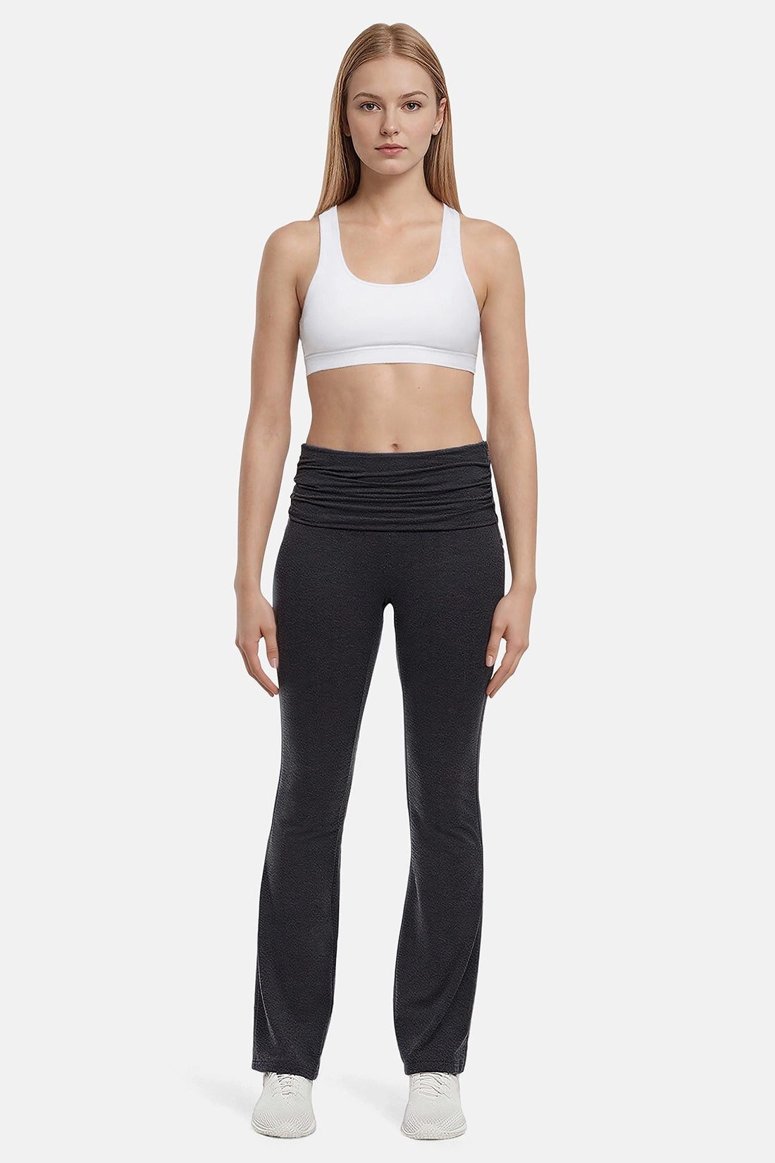 Woman wearing a white sports bra and black yoga pants on a white background