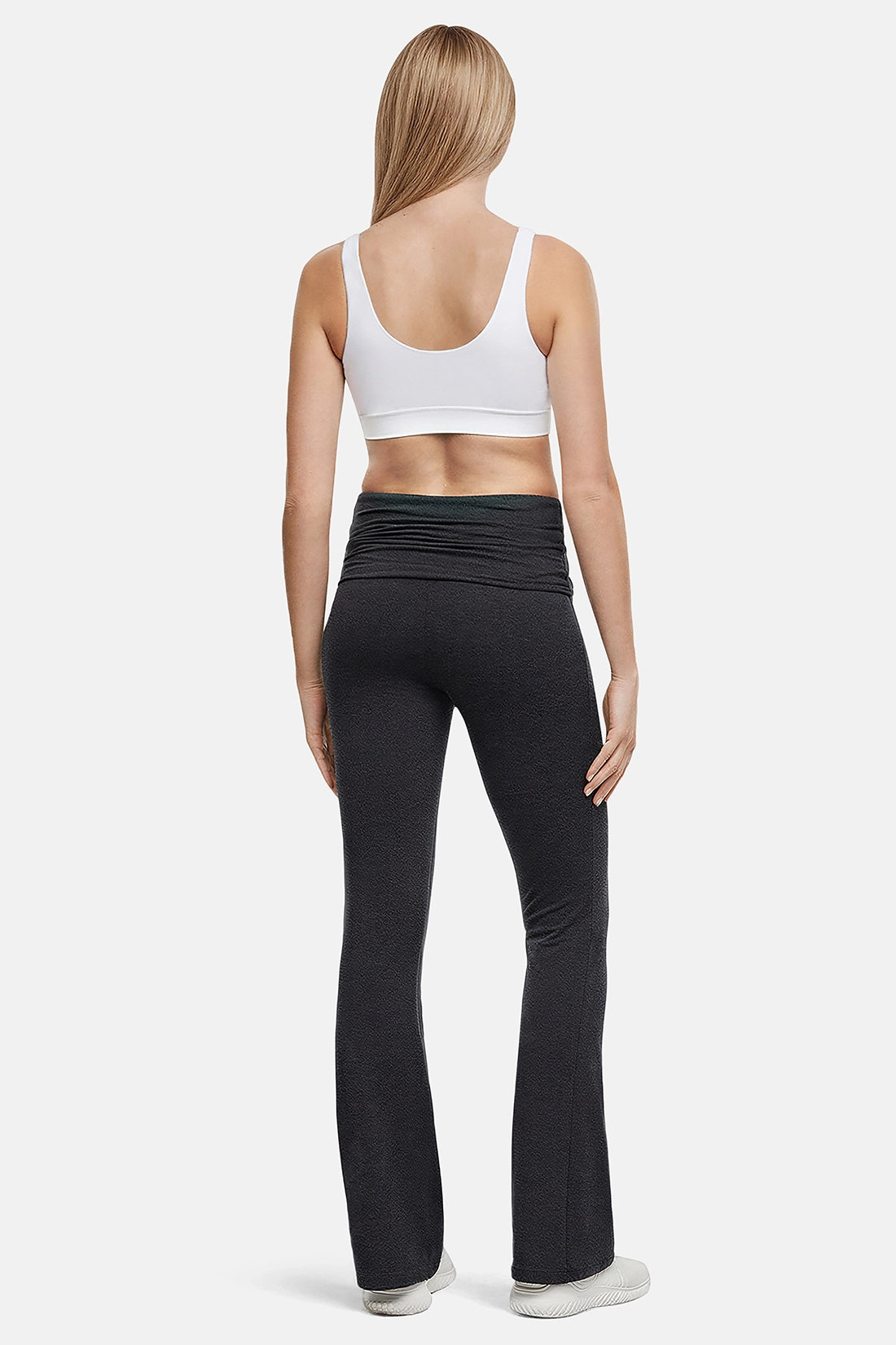 Back of woman wearing a white sports bra and black yoga pants on a white background