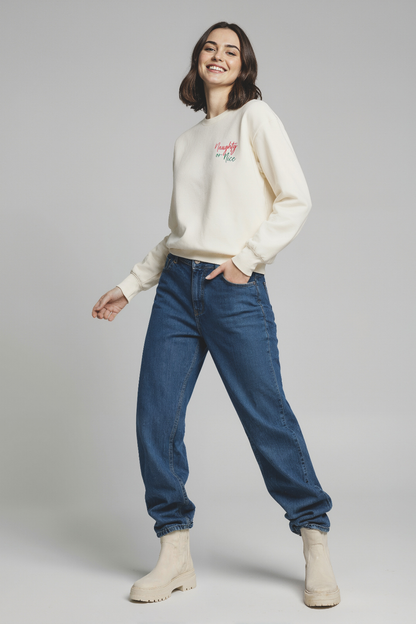 Woman wearing a cream sweater with text and blue jeans on a gray background