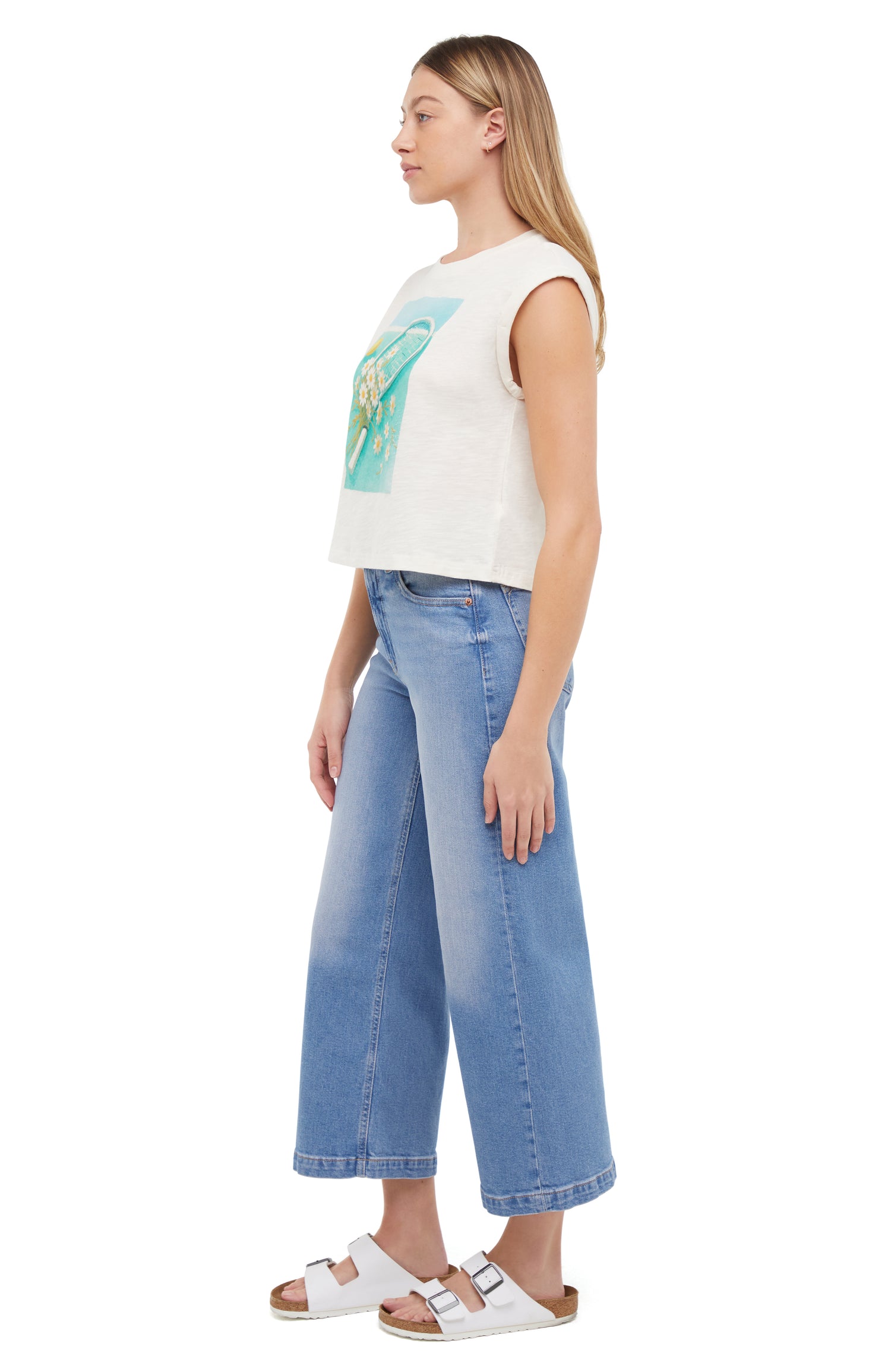 Side view of a woman wearing a white sleeveless shirt with a tennis racket and flowers design, standing against a white background.