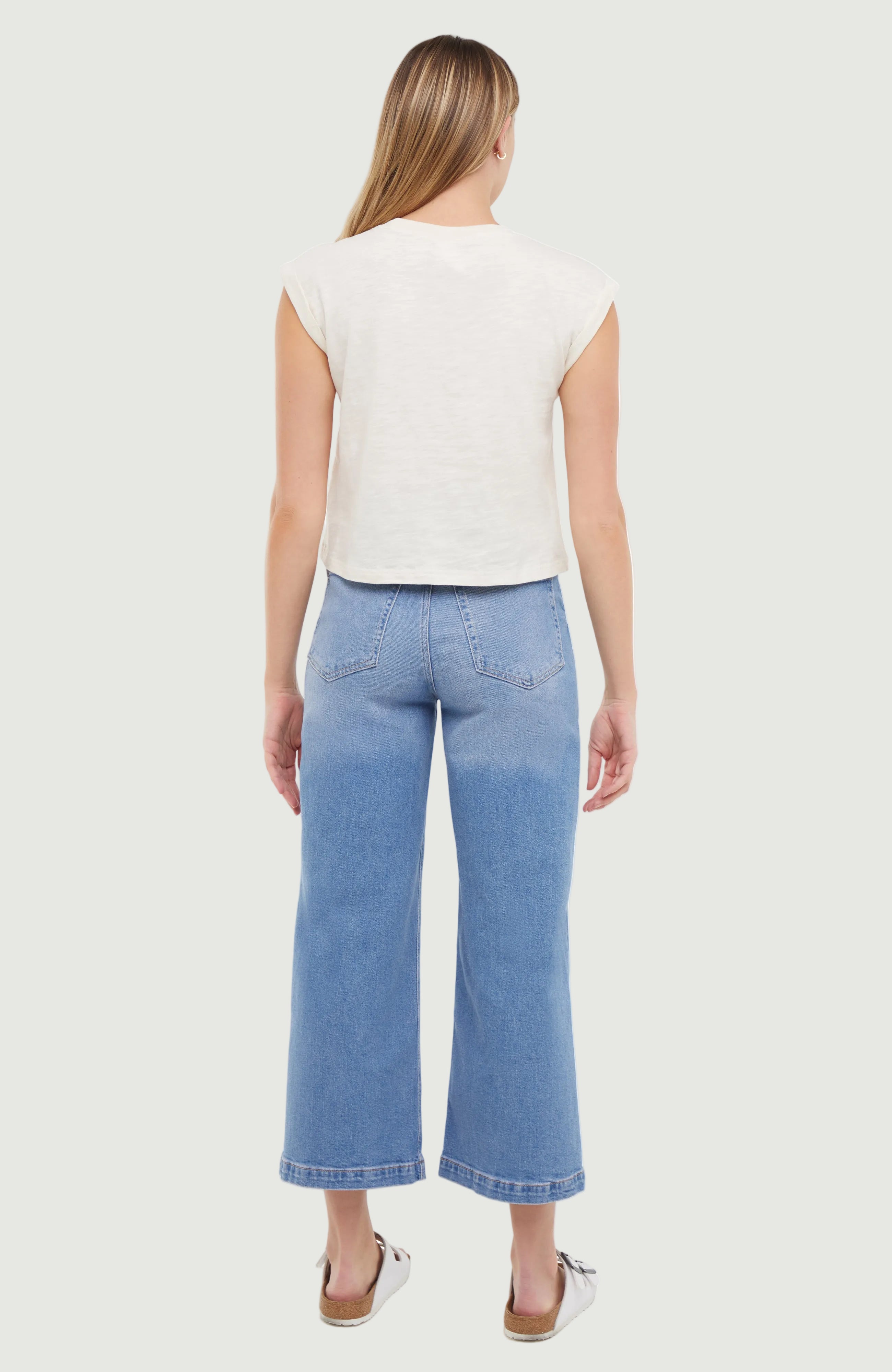 Back of woman wearing a white top and light blue jeans on a white background