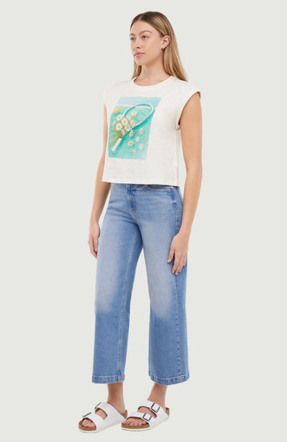 Woman wearing a white sleeveless shirt with a tennis racket and flowers design, standing against a white background.